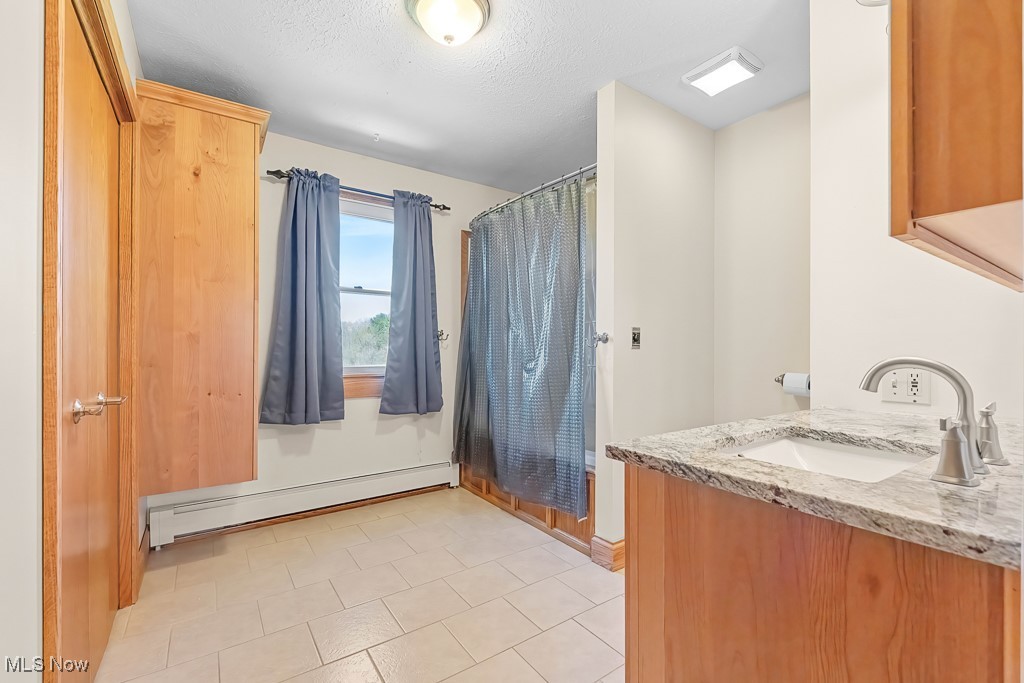 8690 Friendsville Road Lodi, OH 44254 - Photo 27 of 50 Full bathroom with a baseboard heating unit, vanity, baseboards, a textured ceiling, and a shower with shower curtain