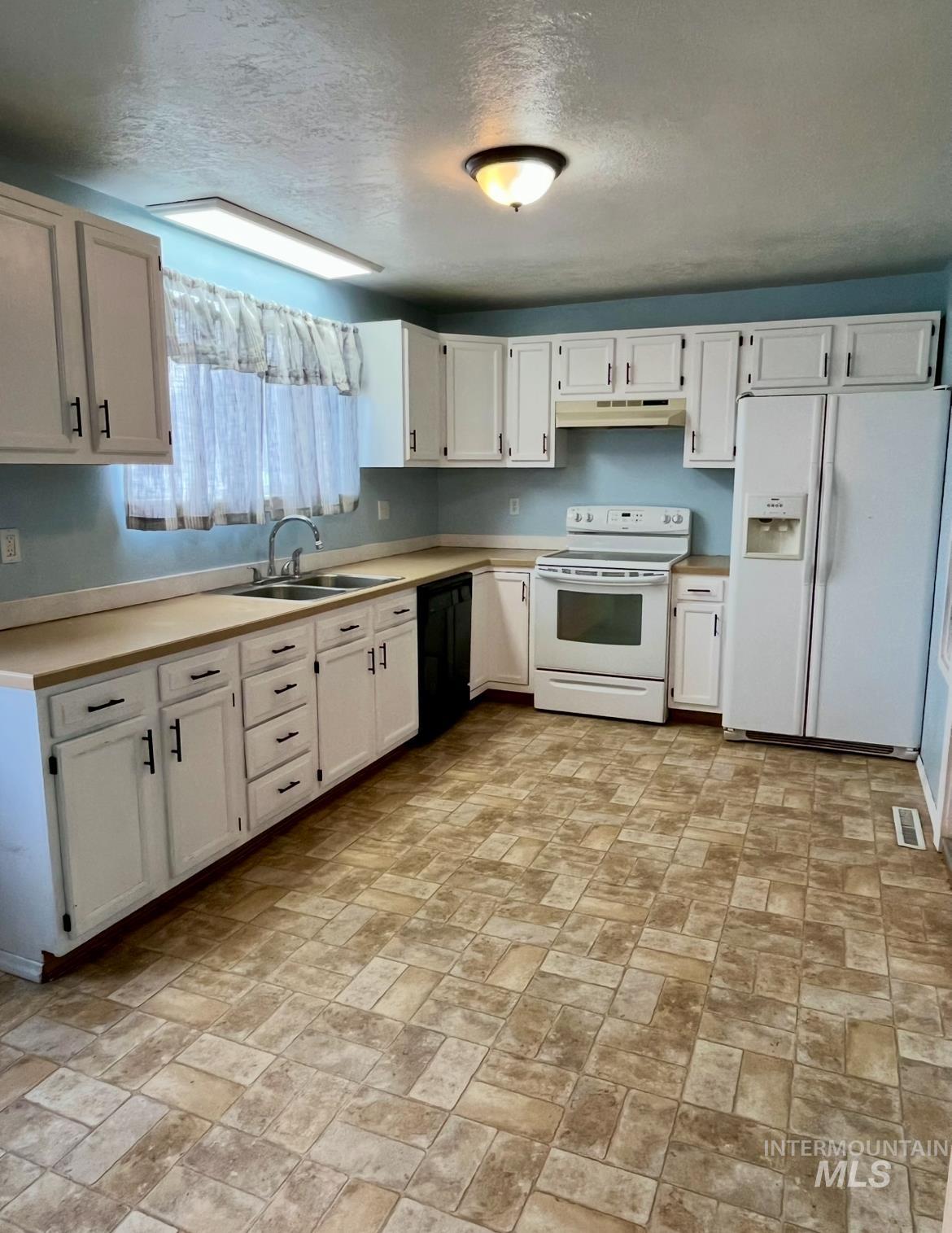 503 Stevens Avenue Filer, ID 83328 - Photo 2 of 13 Kitchen featuring white appliances, light countertops, white cabinets, a textured ceiling, and brick patterned flooring