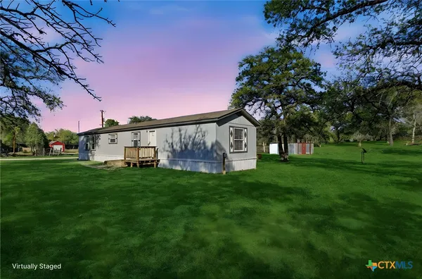 a view of a white house with a big yard plants and large trees