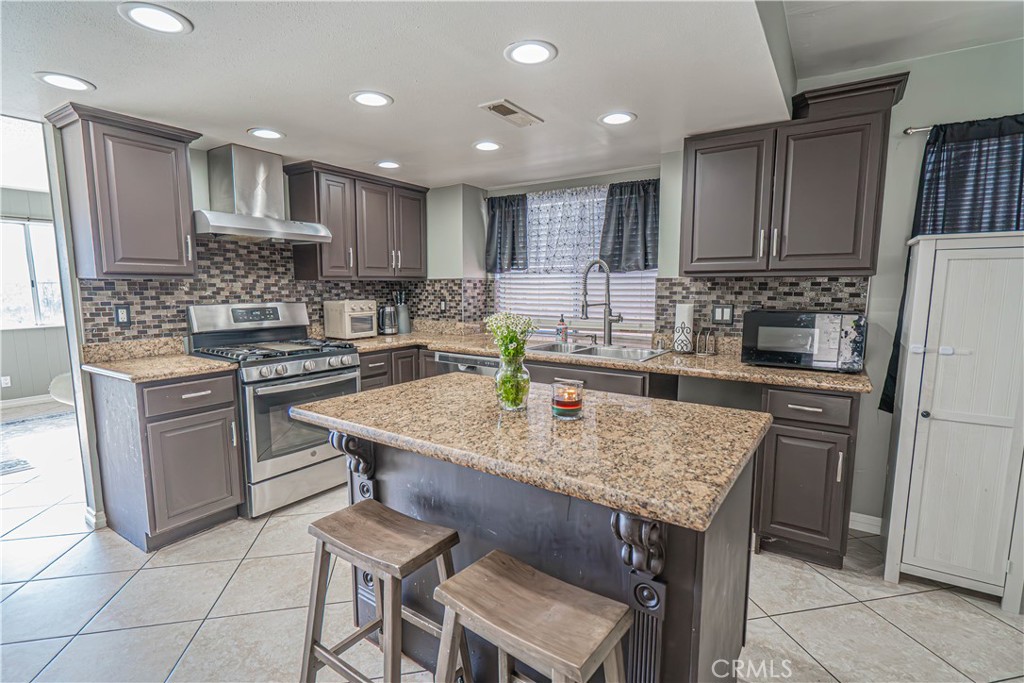 28076 Wildwind Road Canyon Country, CA 91351 - Photo 13 of 48 a kitchen with kitchen island granite countertop wooden cabinets a stove a sink and a center island