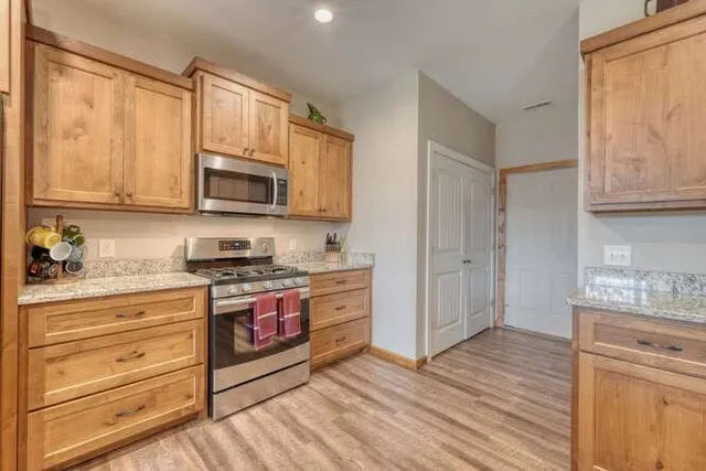 a kitchen with stainless steel appliances granite countertop a stove top oven a refrigerator and a sink with wooden floor