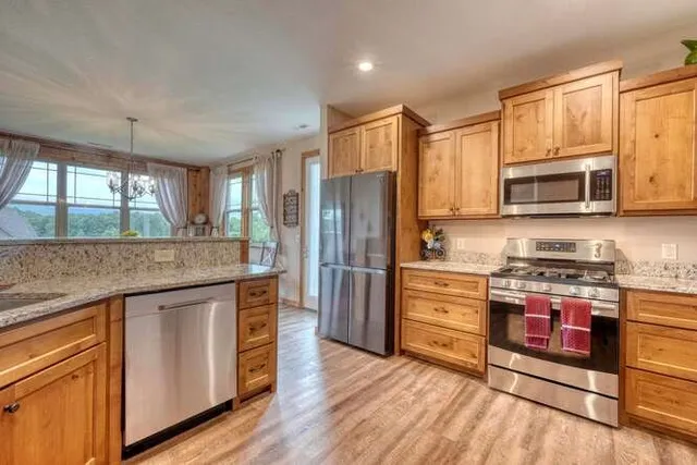 a kitchen with stainless steel appliances granite countertop wooden cabinets a sink a stove a dining table and chairs