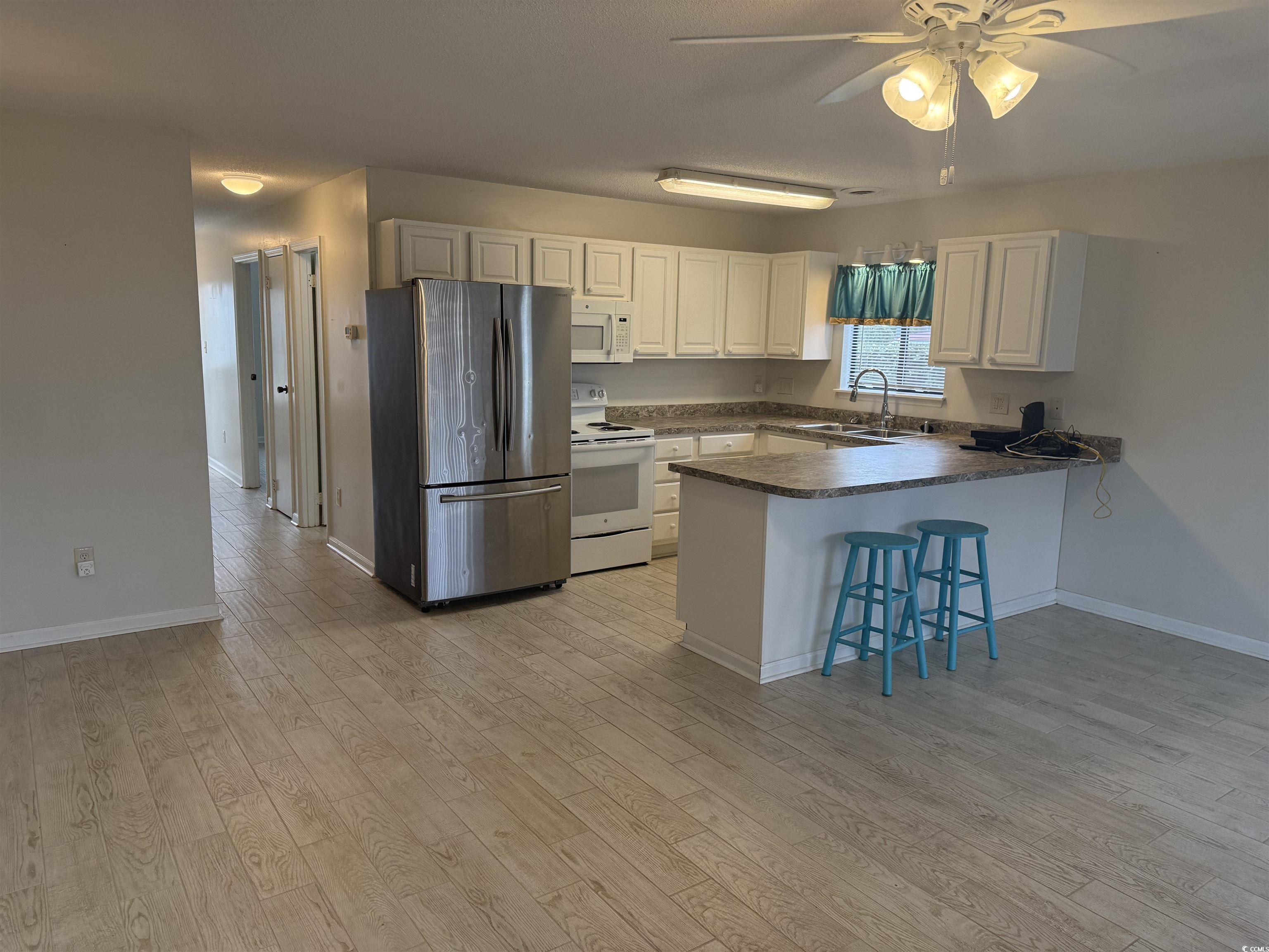 1850 Colony Drive, Unit 2S Myrtle Beach, SC 29575 - Photo 5 of 38 Kitchen featuring dark countertops, white appliances, a breakfast bar, a peninsula, and white cabinets