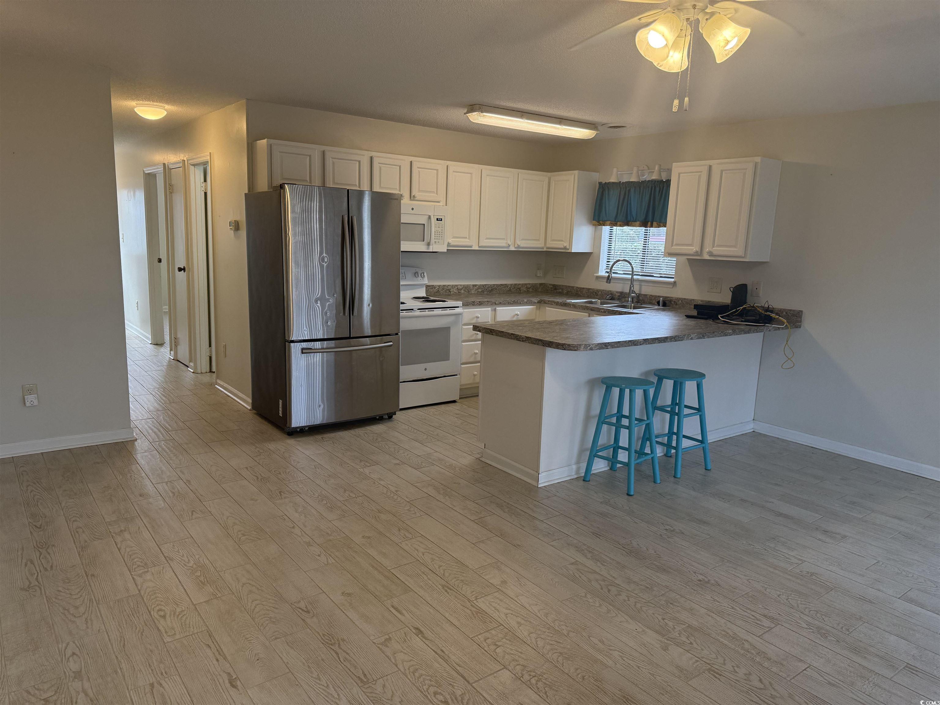 1850 Colony Drive, Unit 2S Myrtle Beach, SC 29575 - Photo 8 of 38 Kitchen with dark countertops, white appliances, a peninsula, a kitchen bar, and white cabinets