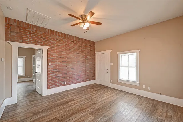 an empty room with wooden floor fan and windows