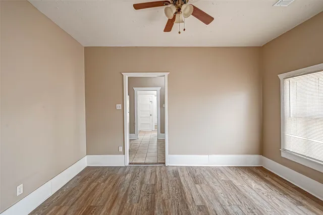 an empty room with wooden floor chandelier fan and windows