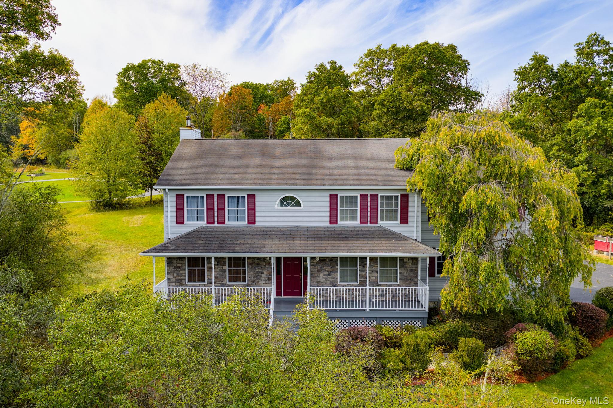 Traditional-style house featuring a porch, stone siding, a front yard, and a chimney