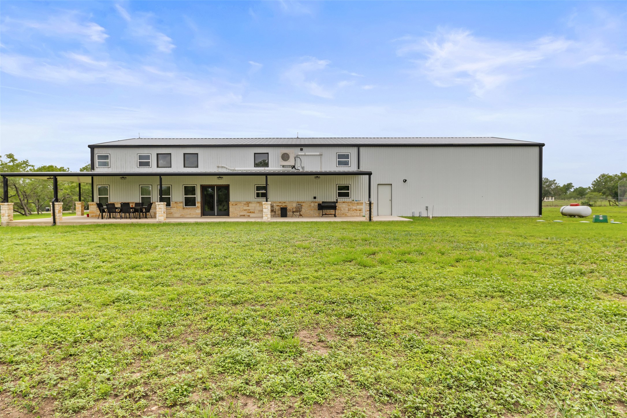 664 Martindale Falls Road Martindale, TX 78655 - Photo 16 of 21 Expansive rear exterior featuring a covered patio with stone-clad columns, multiple sliding glass doors, and a combination of horizontal siding and stone veneer