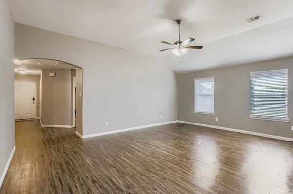 an empty room with wooden floor ceiling fan and windows