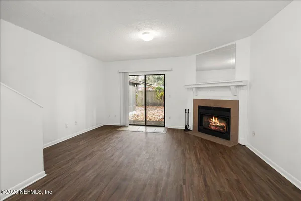 a view of an empty room with wooden floor fireplace and a window