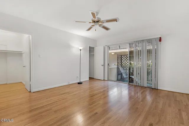 a view of an empty room with wooden floor and a ceiling fan