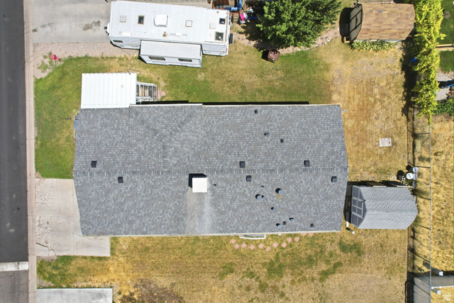 2491 Highway 89, Unit 614 Pleasant View, UT 84404 - Photo 27 of 27 Property featuring a gray asphalt shingle roof, a concrete driveway, a rear yard with a storage shed, and mature trees on the perimeter