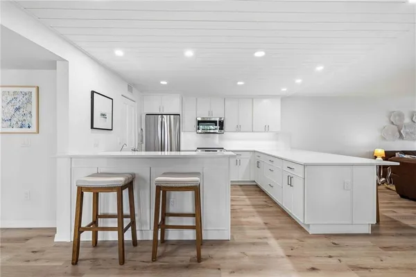 a large white kitchen with wooden floor and stainless steel appliances