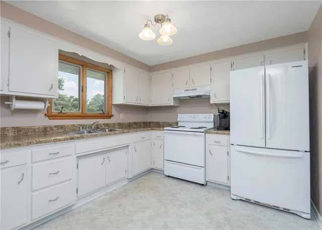 a kitchen with granite countertop white cabinets white appliances a sink and a window