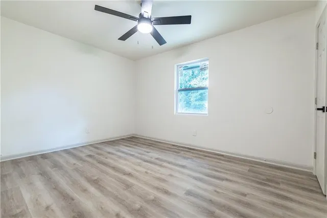 an empty room with wooden floor ceiling fan and windows