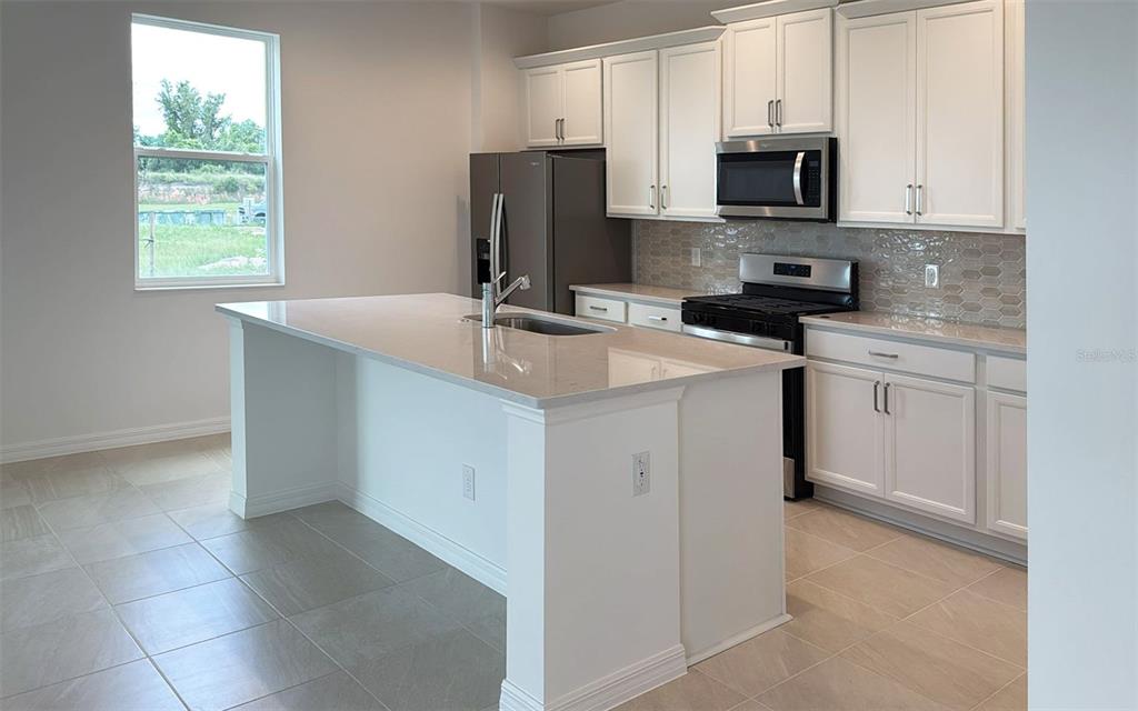 6867 Spanish Imperial Street Howey-in-the-Hills, FL 34737 - Photo 8 of 20 a kitchen with stainless steel appliances a sink a stove a microwave a sink a refrigerator and cabinets