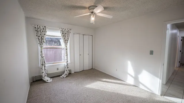 an empty room with chandelier fan and windows