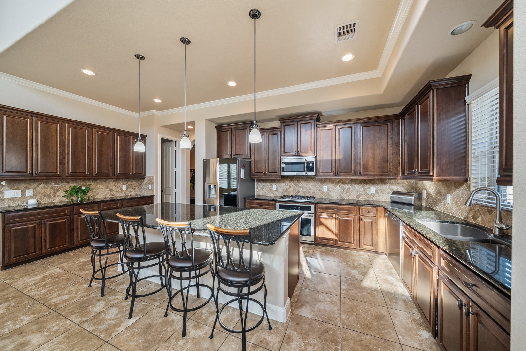 4747 Abercorn Street Rosharon, TX 77583 - Photo 16 of 46 This spacious kitchen features elegant dark wood cabinetry, granite countertops, and a large center island with bar seating. It includes modern stainless steel appliances, tile flooring, and ample natural light, creating a warm and inviting atmosphere.
