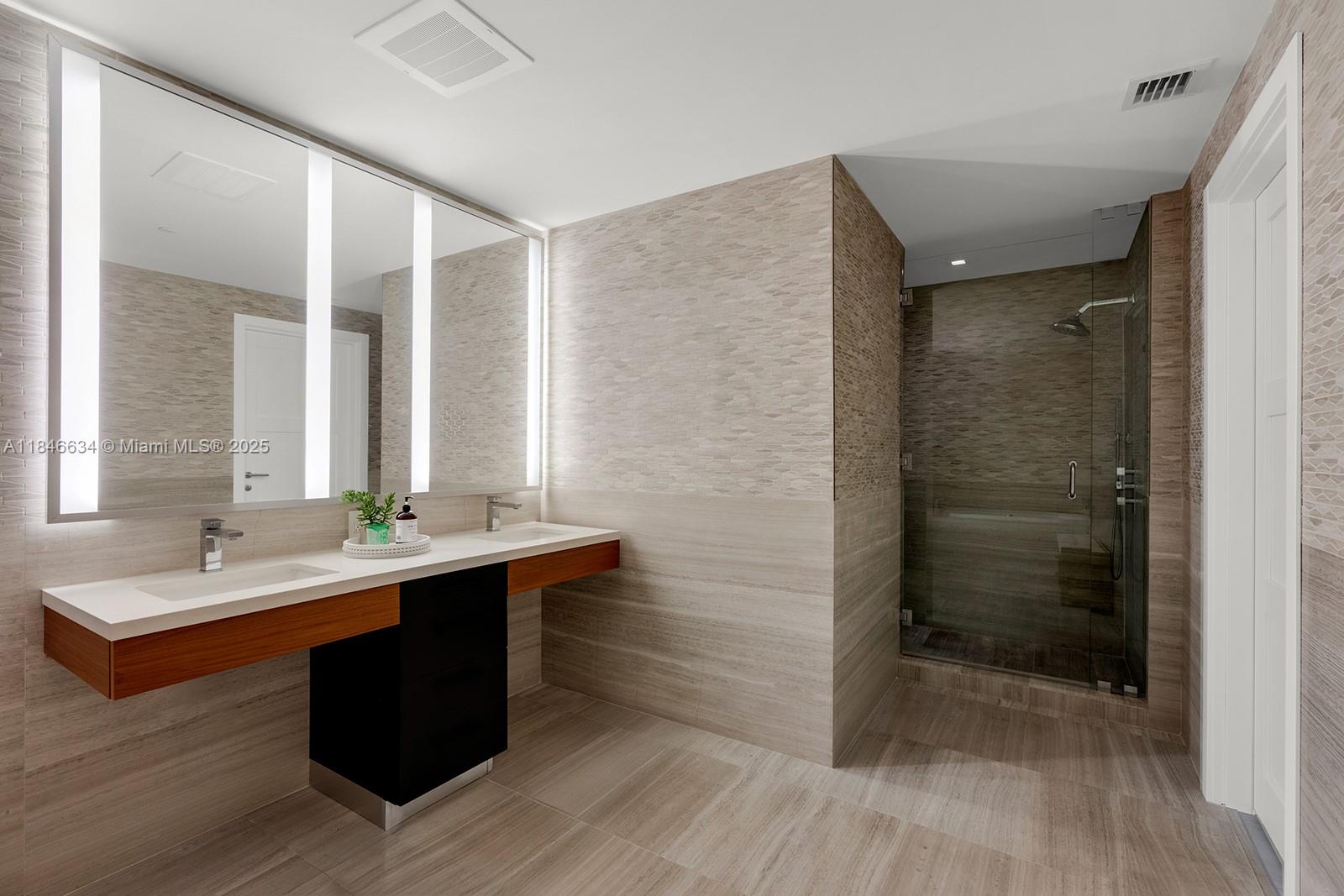 1 Collins Avenue, Unit 605 Miami Beach, FL 33139 - Photo 14 of 33 a bathroom with a double vanity sink a large mirror and shower