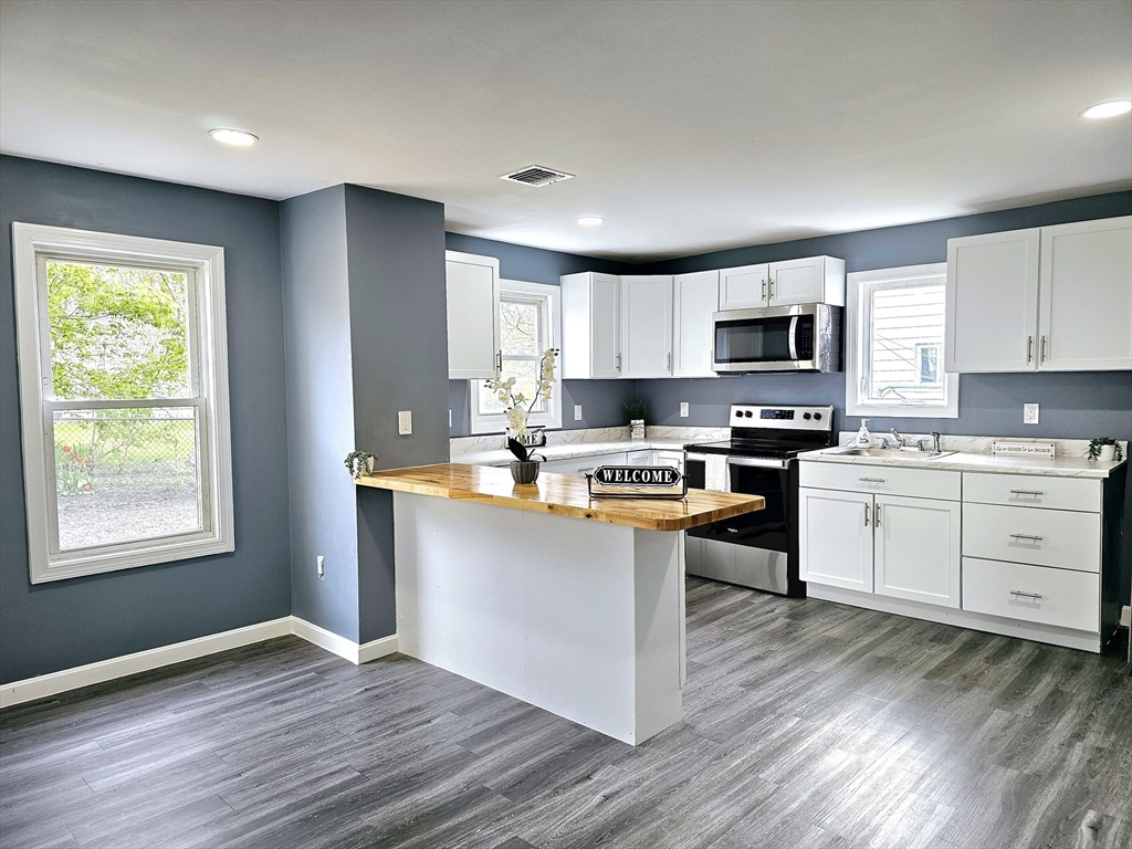 9 Wellington Street Webster, MA 01570 - Photo 3 of 37 a kitchen with kitchen island granite countertop a stove top oven a sink dishwasher and white cabinets with wooden floor
