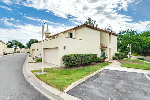 a view of a white house with a yard plants and large tree
