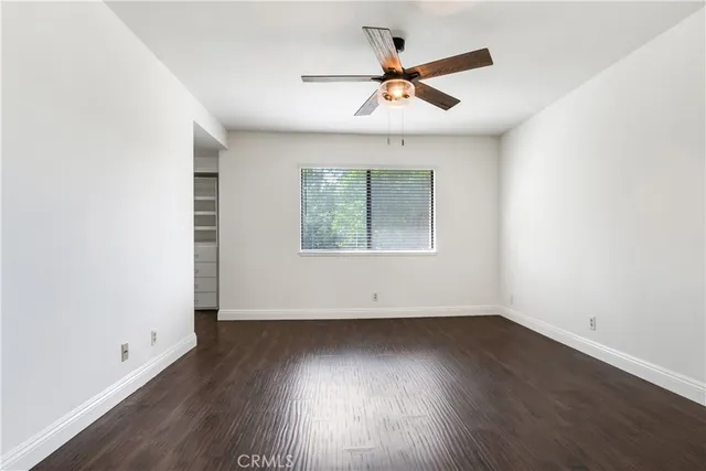 an empty room with wooden floor ceiling fan and windows