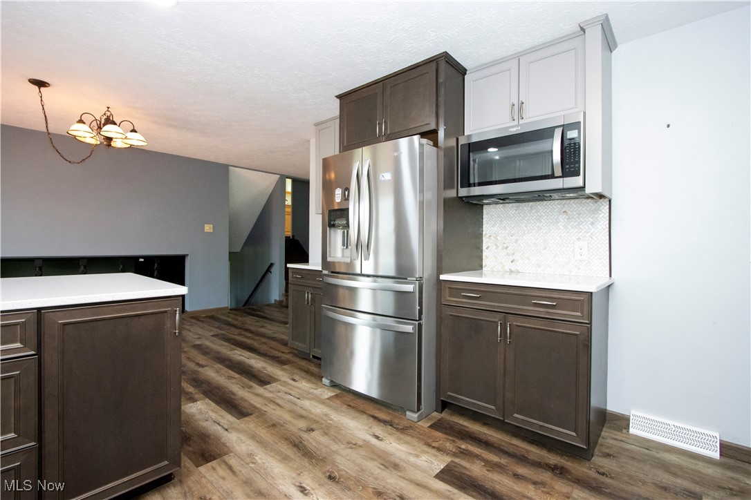 Kitchen with appliances with stainless steel finishes, dark wood-style flooring, dark brown cabinets, backsplash, and a textured ceiling