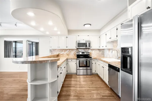 a large kitchen with stainless steel appliances kitchen island granite countertop a refrigerator a stove top oven a sink dishwasher and white cabinets with wooden floor