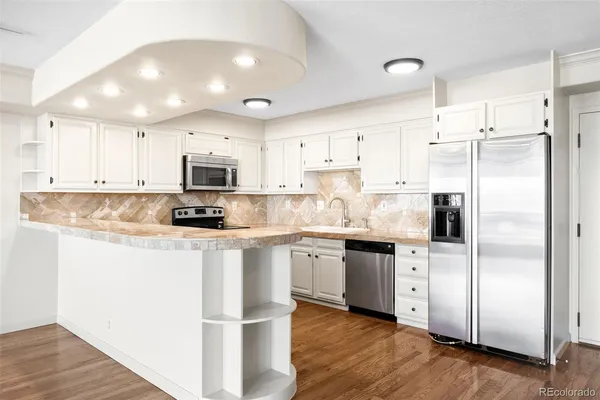 a kitchen with stainless steel appliances granite countertop a refrigerator a sink dishwasher a stove and white cabinets with wooden floor