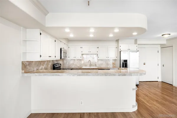 a large white kitchen with kitchen island a sink a center island stainless steel appliances and a refrigerator