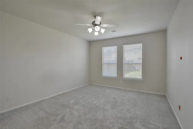 an empty room with chandelier fan and windows