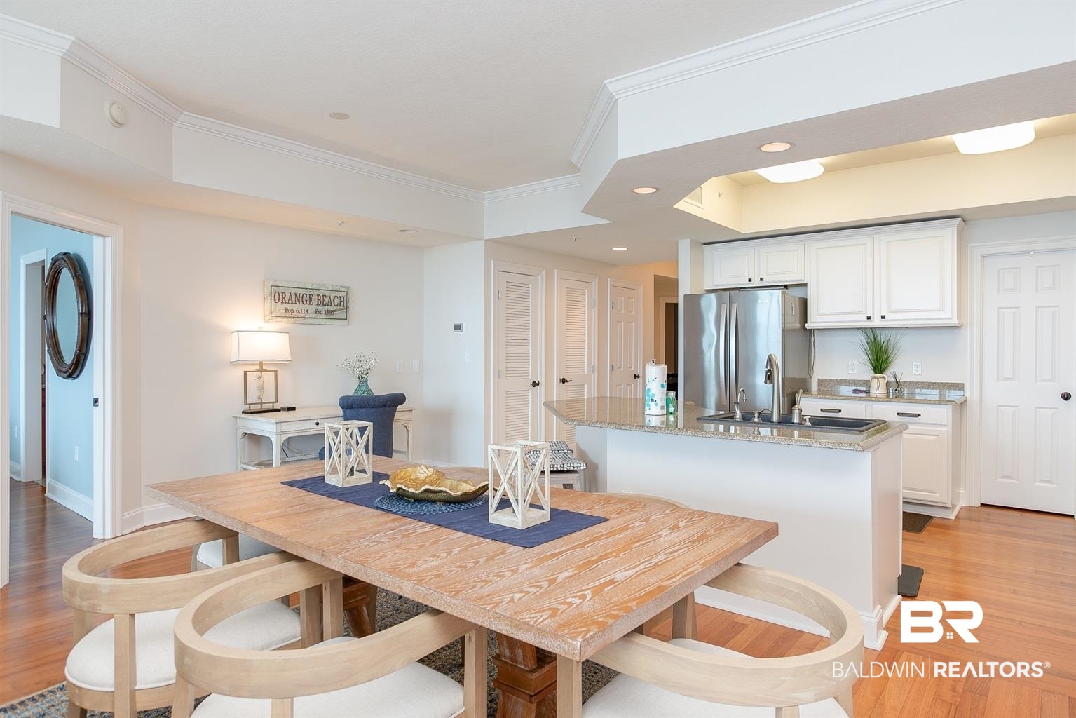 27800 Canal Road, Unit 411 Orange Beach, AL 36561 - Photo 13 of 49 Open-concept dining and kitchen area featuring wood-finish flooring, white cabinetry, stainless steel appliances, and an integrated kitchen island with a sink