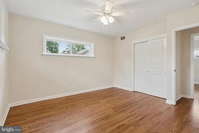 an empty room with wooden floor ceiling fan and windows