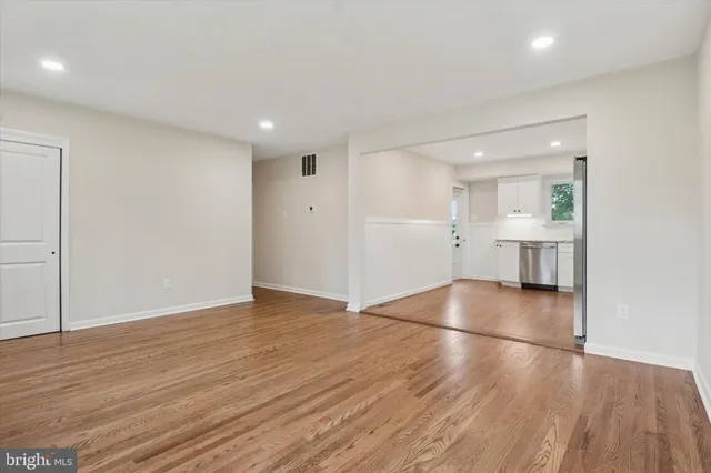 a view of empty room with wooden floor and kitchen
