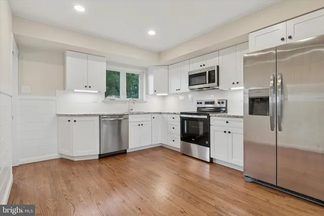 a kitchen with stainless steel appliances granite countertop a stove a sink dishwasher a refrigerator and a oven with wooden floors