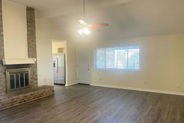 an empty room with wooden floor fireplace and windows