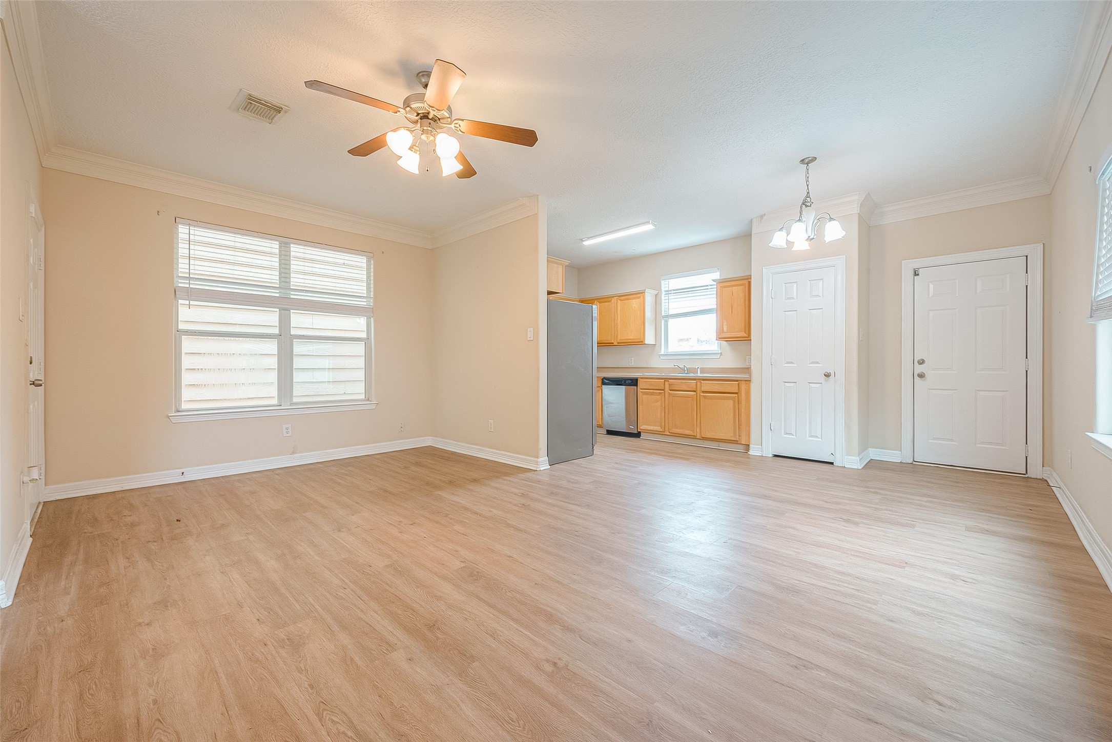 10355 Panther Point Drive Houston, TX 77099 - Photo 11 of 44 This photo showcases a bright, open-plan living and kitchen area with light wood flooring. The kitchen features natural wood cabinets and stainless steel appliances. Large windows and a ceiling fan enhance the space, providing a welcoming atmosphere.