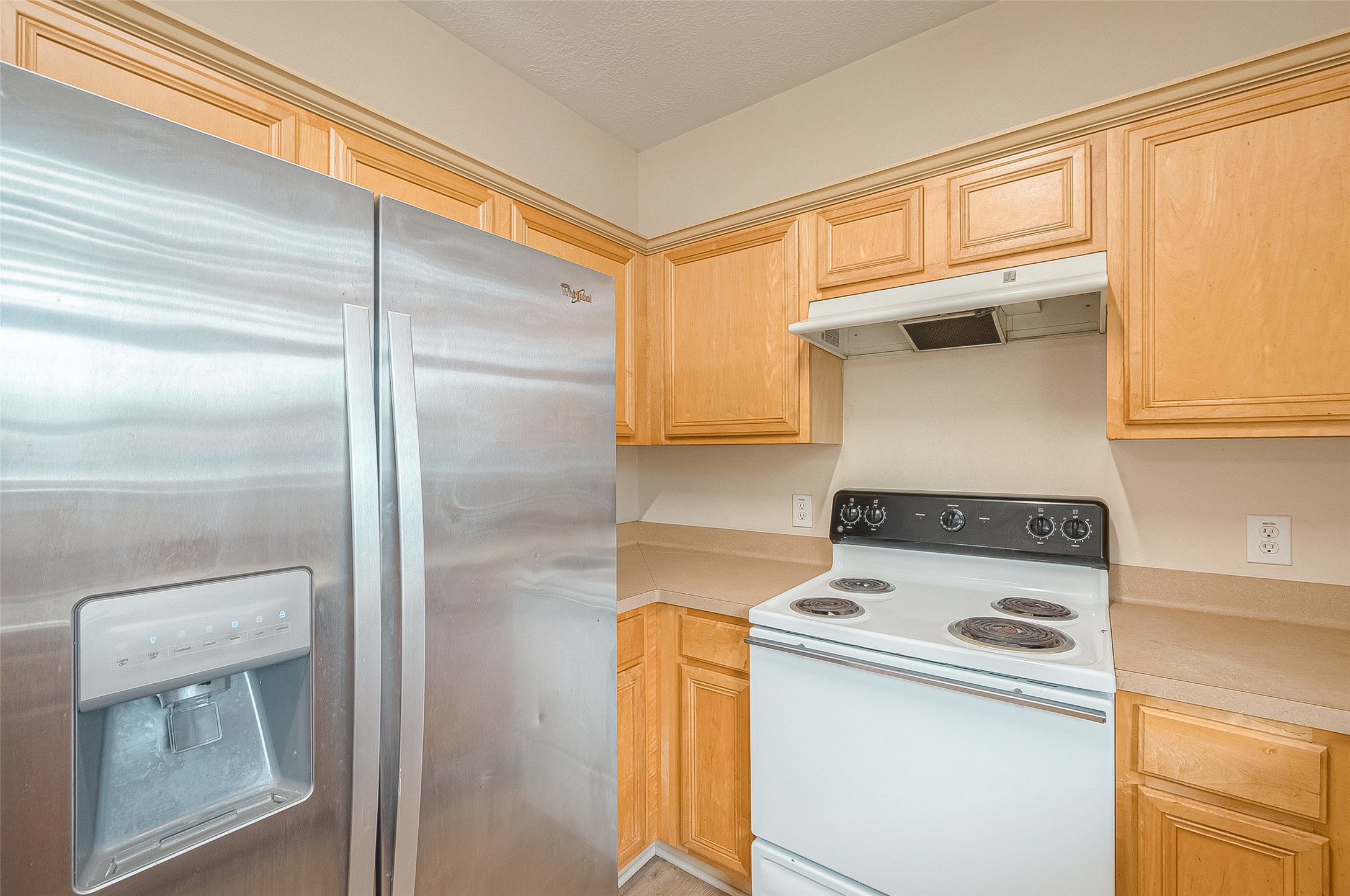 10355 Panther Point Drive Houston, TX 77099 - Photo 19 of 44 This kitchen features light wood cabinetry, a stainless steel refrigerator with a water dispenser, and a white electric stove with a range hood. The counters offer a clean, neutral look.