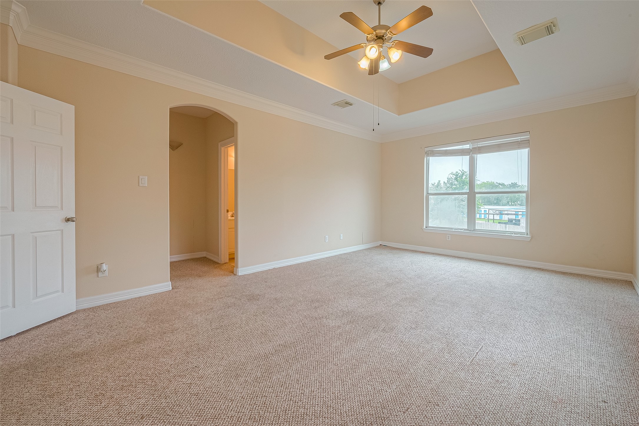 10355 Panther Point Drive Houston, TX 77099 - Photo 23 of 44 This spacious bedroom features neutral carpeting, a tray ceiling with a ceiling fan, and ample natural light from a large window. An open doorway leads to an en-suite bathroom.