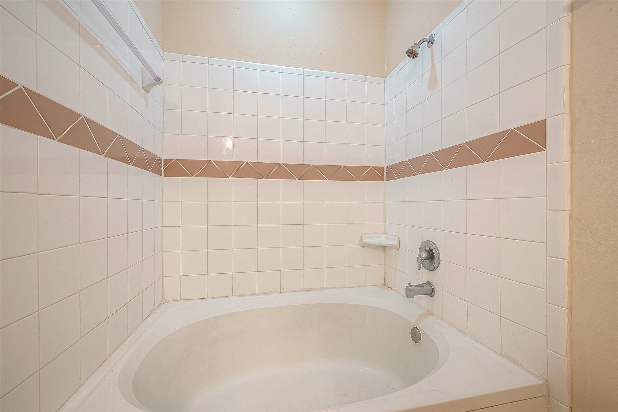 10355 Panther Point Drive Houston, TX 77099 - Photo 29 of 44 This bathroom features a spacious, white-tiled bathtub with a showerhead. The walls are accented with a decorative tile border in a neutral tone, and a built-in soap dish adds convenience.