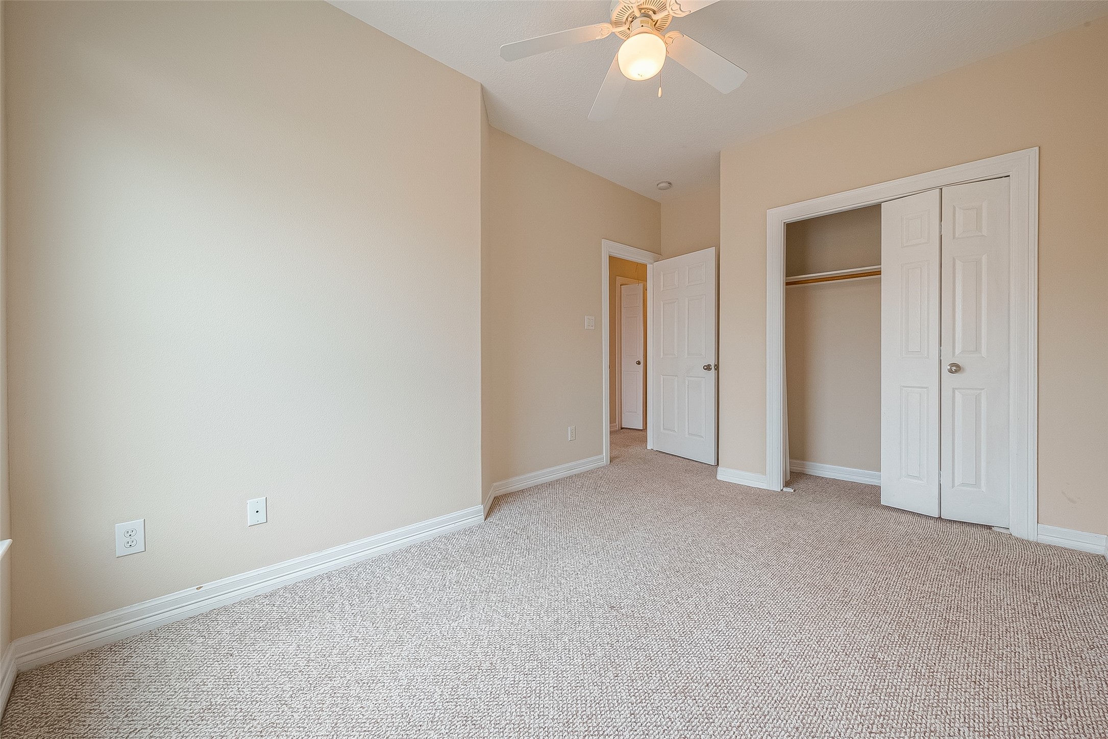 10355 Panther Point Drive Houston, TX 77099 - Photo 35 of 44 This photo shows a bright, neutral-toned bedroom with carpeted flooring, a ceiling fan, and a closet with double doors. The space is well-lit and inviting, offering a blank canvas for personalization.