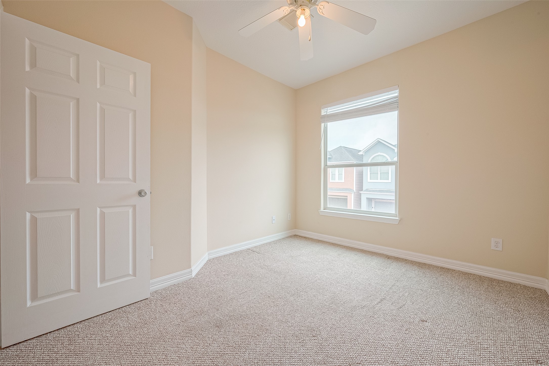 10355 Panther Point Drive Houston, TX 77099 - Photo 37 of 44 This photo shows a bright, empty room with neutral walls, carpeted flooring, a window with a view of neighboring houses, and a ceiling fan.