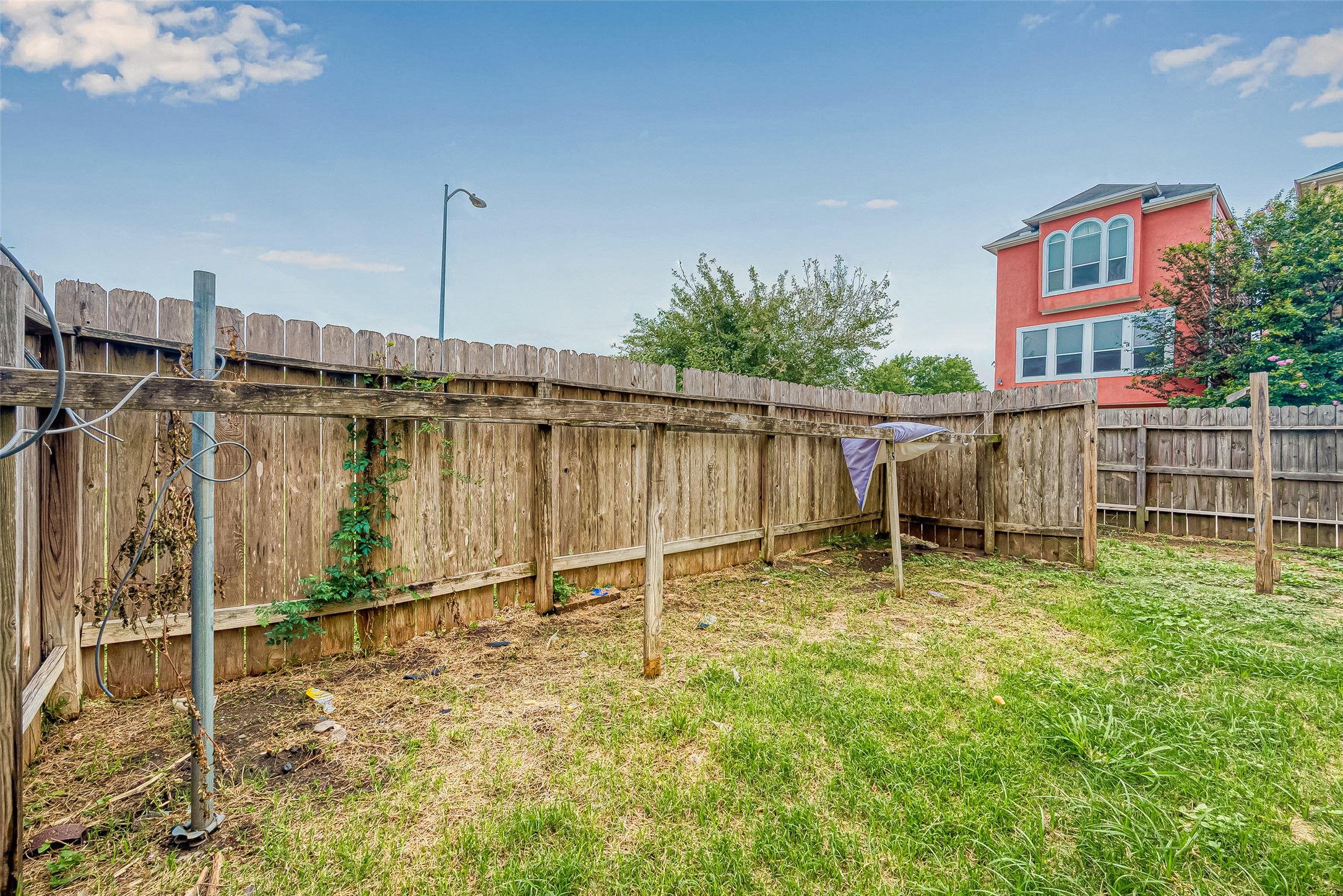 10355 Panther Point Drive Houston, TX 77099 - Photo 41 of 44 This photo shows a small, fenced backyard with a wooden fence and some greenery. It appears to have a clothesline and offers a view of a neighboring house. The area is grassy with some patchy spots, suggesting potential for landscaping.