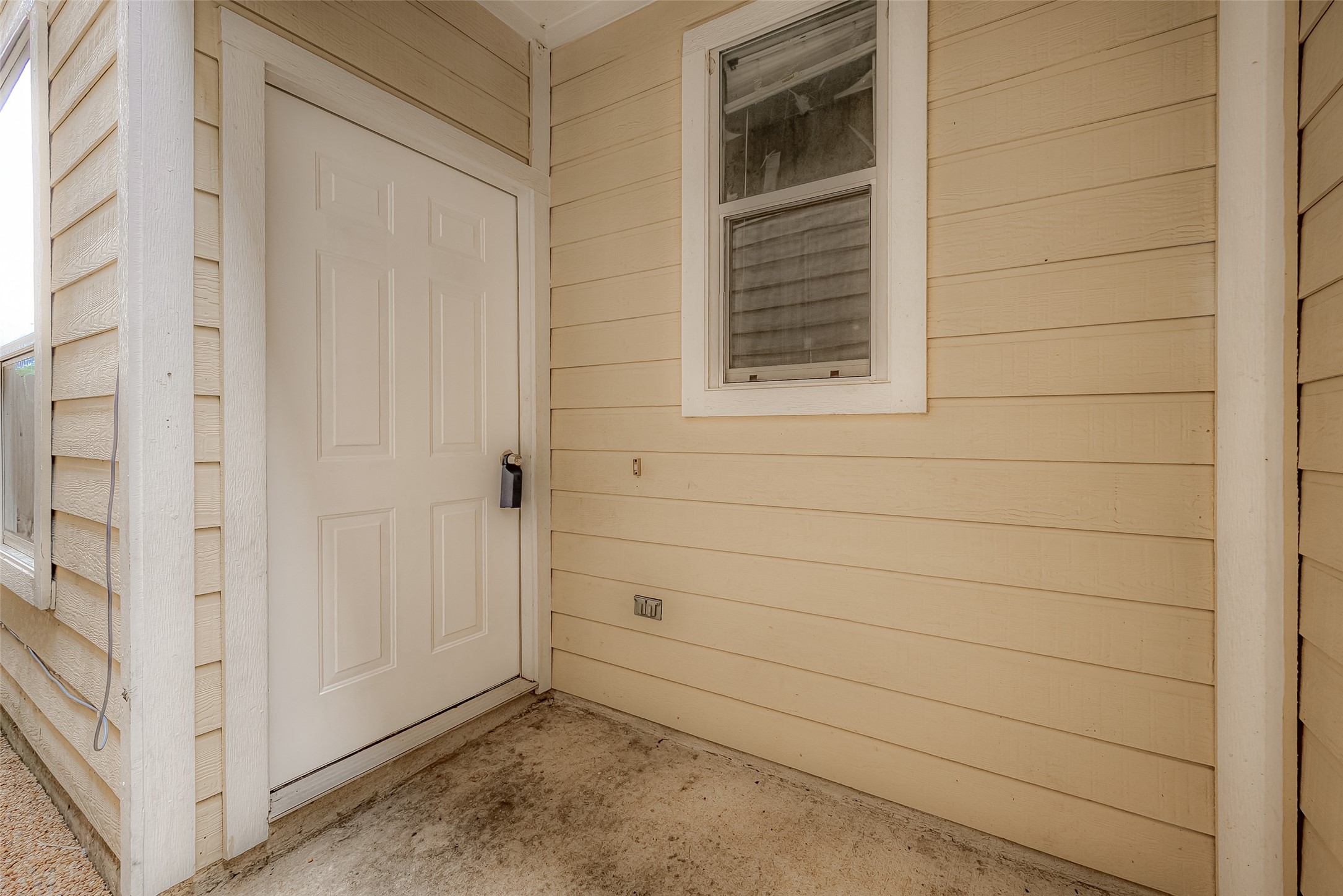 10355 Panther Point Drive Houston, TX 77099 - Photo 7 of 44 This photo features a small, covered entryway with beige siding, a white door, and a single window. The area is compact and functional, offering a simple entrance to the home.