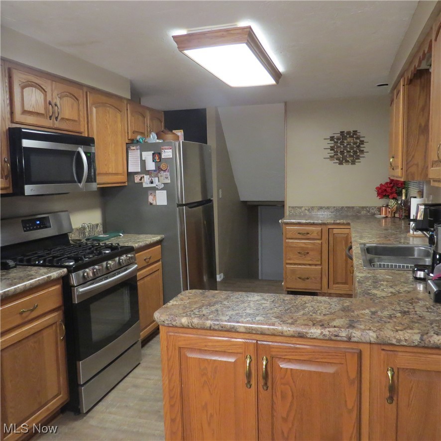 46580 Middle Ridge Road Amherst, OH 44001 - Photo 28 of 38 Kitchen featuring stainless steel appliances, a peninsula, wood finish cabinetry, light stone countertops, and light wood-style floors