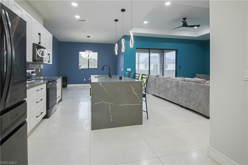 3902 4th Street Southwest Lehigh Acres, FL 33976 - Photo 6 of 34 Modern kitchen with an expansive island featuring an integrated sink, sleek pendant lighting, stainless steel appliances, and white cabinetry