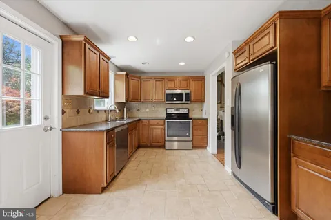 a kitchen with stainless steel appliances granite countertop a refrigerator a sink dishwasher a stove top oven a kitchen island and chairs with wooden floor