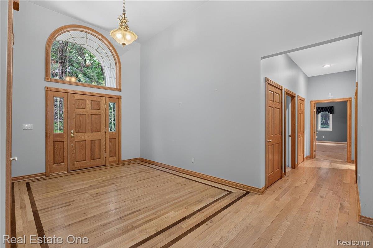 425 Courtney Road Leonard, MI 48367 - Photo 7 of 89 Foyer featuring a grand arched transom window, a six-panel wood entry door with sidelights, and light wood-finish flooring with a contrasting border