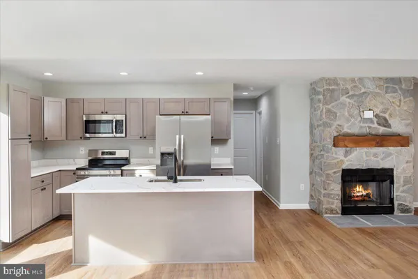 a kitchen with stainless steel appliances granite countertop a stove a refrigerator a sink and a fireplace with wooden floor