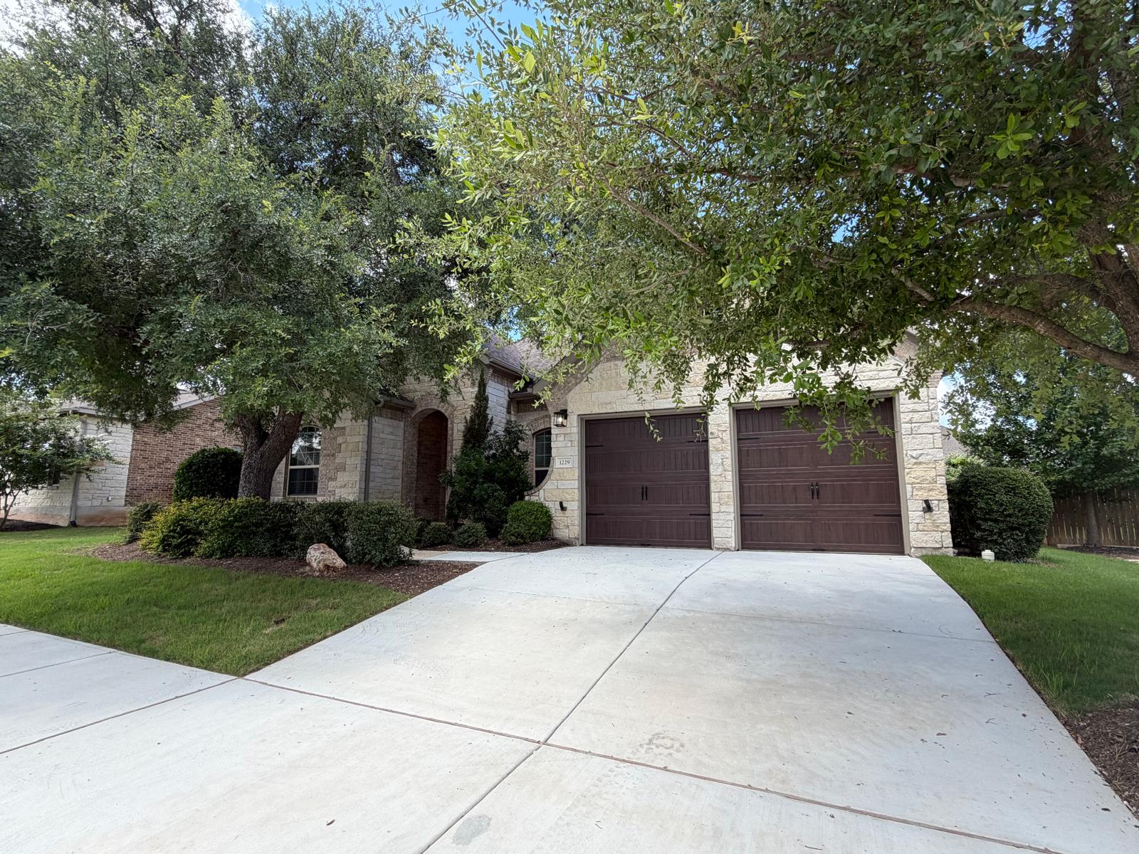1229 Terrace View Drive Georgetown, TX 78628 - Photo 3 of 17 Mature trees frame this charming residence, boasting a concrete driveway and an inviting stone facade.